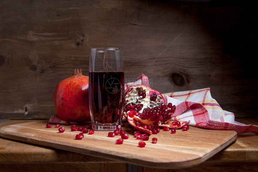 成熟的红石榴和木制背景上的新鲜鲁迪汁玻璃的组成玻璃中红宝石种子石榴果实和甜图片
