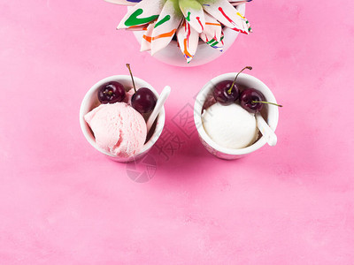 两杯冷冻酸奶冰淇淋勺和粉红色背景的樱桃五颜六色的肉质图片