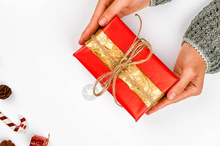 手中的红色和礼品包装用白色上的蝴蝶结针织DIY礼品包装女人的手给了一个包裹的礼物圣诞礼背景图片