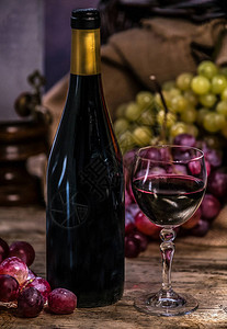 成熟的葡萄红酒杯和木制背景上的一瓶酒图片