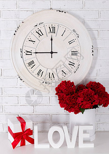 爱情和人节日概念用木字写成爱鲜花礼物和古钟的白砖图片