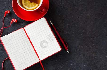黑桌上用笔耳机和茶杯的红色空白笔记本图片