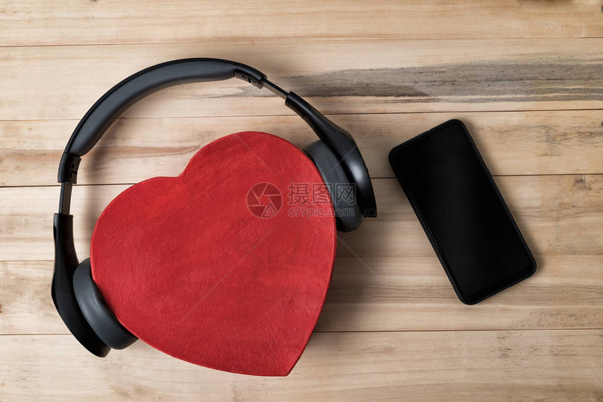 全尺寸无线耳机停在红心形盒子和浅棕色木制桌子上的智能手机图片