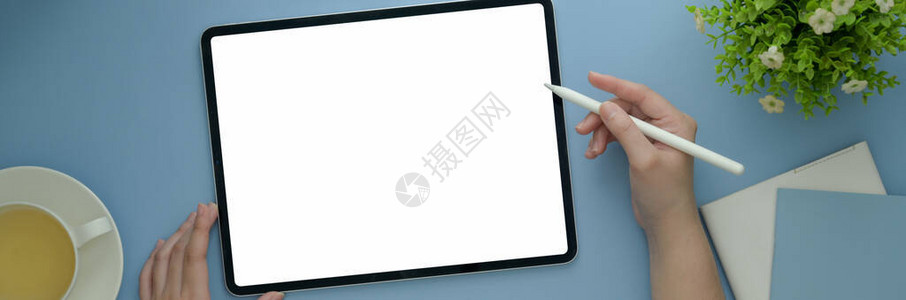 在家工作的妇女自由职业者在轻蓝桌子上用空白屏幕平板打图片