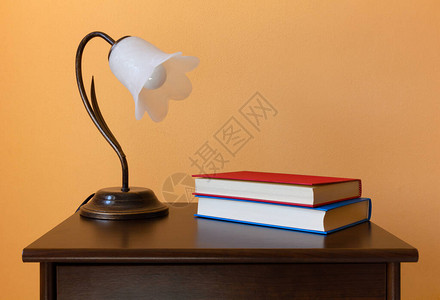 一盏经典的花形灯和木制床头柜上的两本书图片