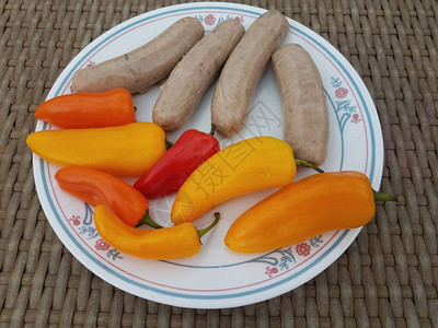 桌上白盘子上的香肠和五颜六色的辣椒图片
