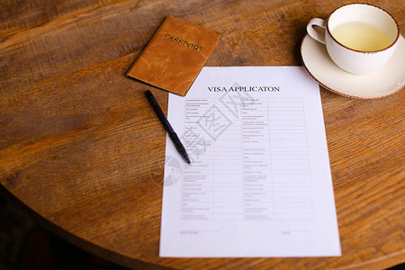 签证申请和护照躺在靠近一杯茶的木桌上执行移民和旅图片