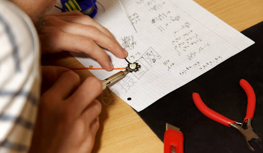 年轻的工程学院生在他的桌子上焊接简单的有线朗伯LED二极管图片