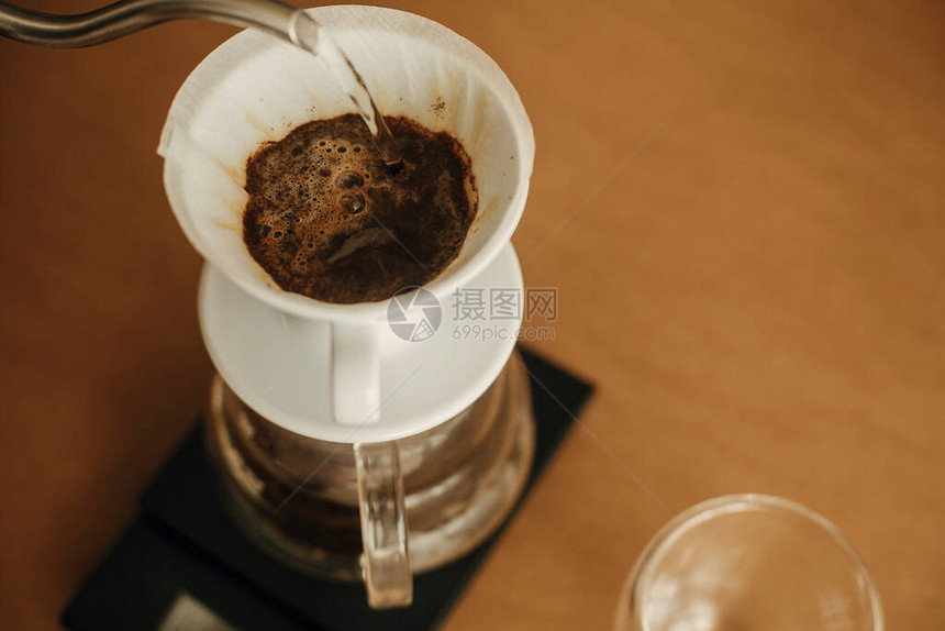 替代咖啡冲泡v60特写咖啡师在棕色背景上制作过滤咖啡将钢壶中的热水倒入过滤器中图片