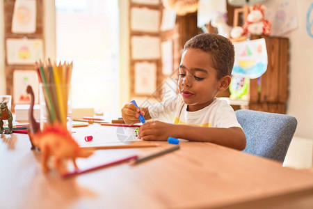 美丽的小孩在幼稚园的书桌上用记分笔坐在绘图片