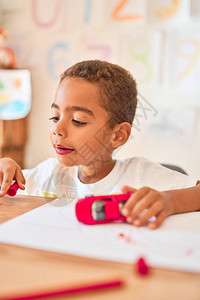 美丽的小孩在幼稚园的书桌上用记分笔坐在绘图片