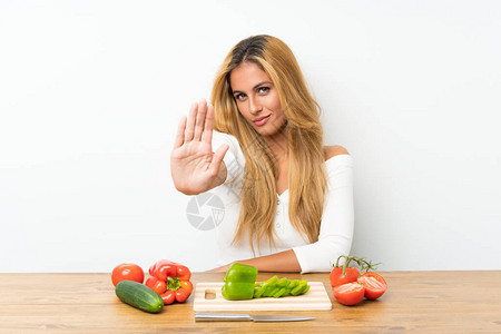 带着蔬菜的金发年轻金发女孩在桌子上图片