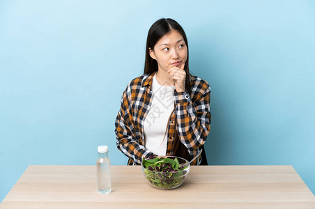 年轻的女孩吃沙拉在寻找时图片