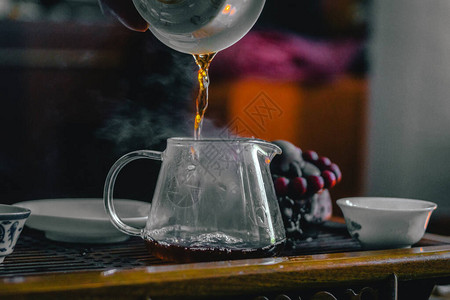 将绿茶从玻璃壶倒到小杯子的手图片