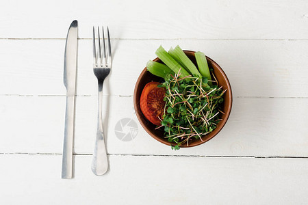 番茄大菜和碗中的微绿色在用餐具制成图片