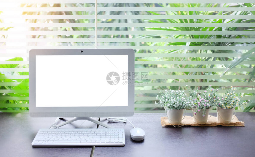 具有工作空间背景的台式计算机和在透明玻璃窗旁有一小桶人工花朵图片
