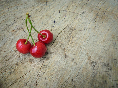 树的锯木剪断上躺着三个红色多汁樱桃绿色花茎躺在树上一个图片