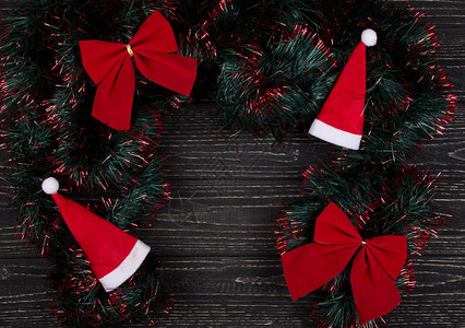 圣诞帽红色圣诞蝴蝶结和绿色和红色金属丝在黑色木质背景上形成框架图片