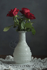 木桌上的白色花瓶中的三朵红玫瑰花边布图片