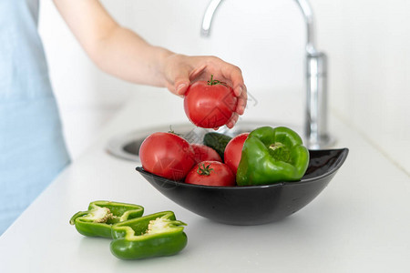 在厨房用蔬菜在碗盘上盛满红熟番茄和煮熟番茄的妇图片