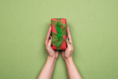 手持红纸包裹的礼物和装饰带有绿色背景带及复制空间的彩图片