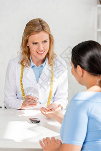 坐在桌边并接受诊所病人血检的微笑营养学家背景图片