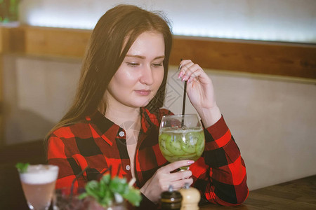 穿着格斗衬衫的女人正喝鸡尾酒从一杯在餐高清图片