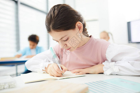 坐在学校书桌旁写作文横向中等合影的黑棕色头发白女图片