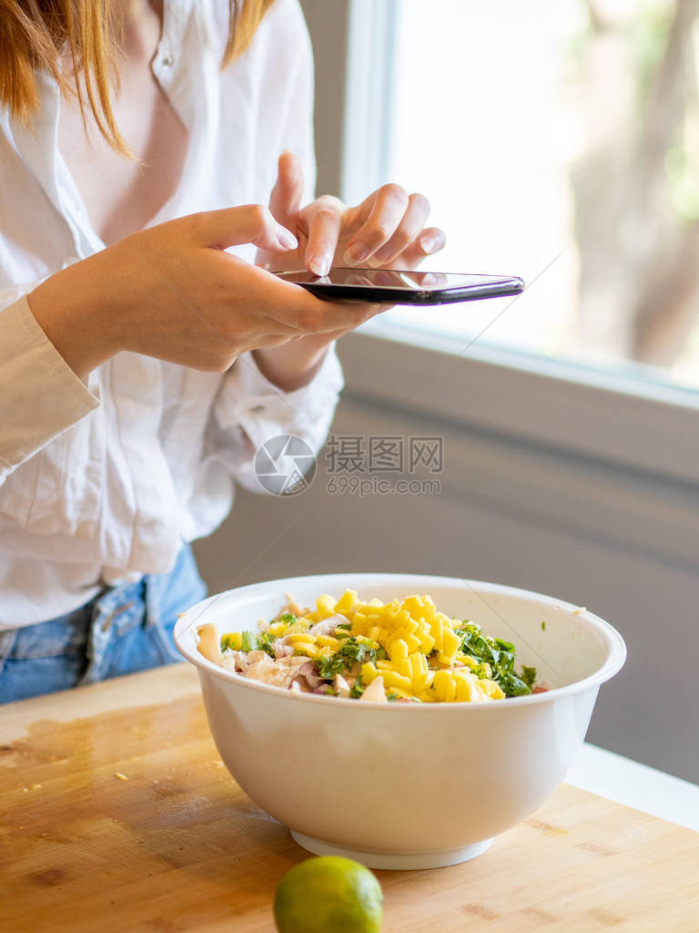 现代厨房里的白种女孩用手机查询她要用蔬图片
