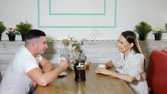 可爱的年轻夫妇在约会期间在舒适餐厅里坐在木制餐桌边图片