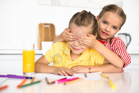 妹纸反击可爱的小孩在桌上用铅笔和书纸蒙着妹的眼睛背景