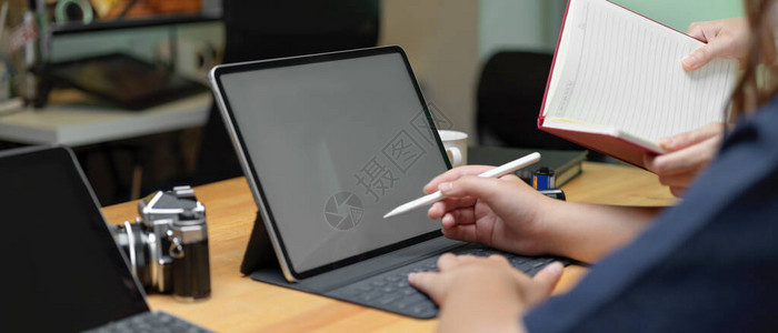 两名女雇员用模拟平板电脑和空白笔记本向她们介绍项目图片
