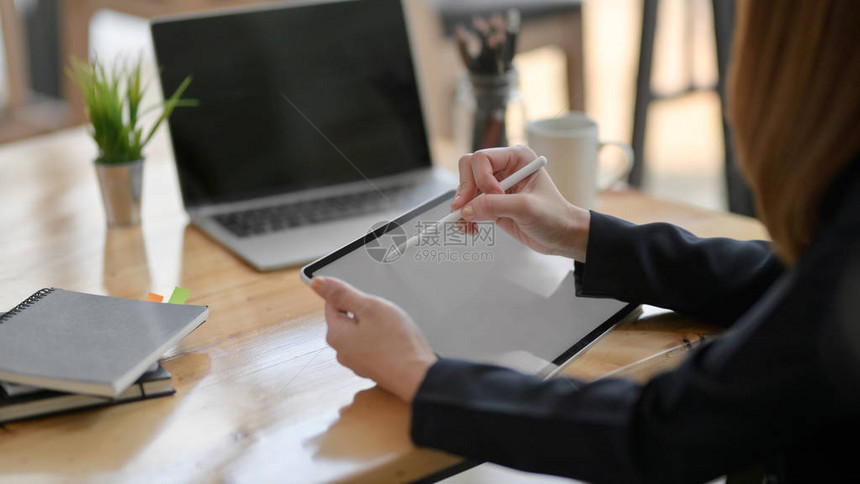 在简单工作场所的木制办公桌上写空白屏幕平板纸上的商业女商人用笔记本电图片