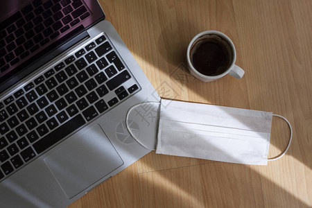 笔记本电脑咖啡和一次口罩放在办公桌上图片