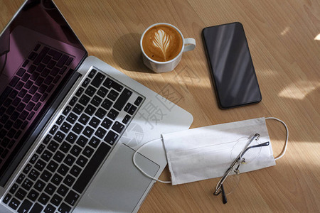 笔记本电脑手机眼镜咖啡和一次口罩放在办公桌上图片