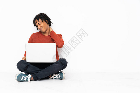 坐在地板上工作并使用笔记本电脑的非洲青年男子因努力而肩膀受疼痛折磨图片