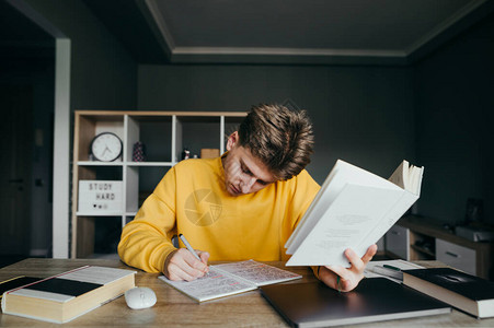 年轻男学生坐在家里舒适房间的桌子旁图片