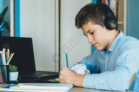 穿着蓝色衬衫的可爱小男孩坐在他房间的桌子后面图片