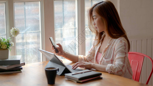 在简单的工作场所的木桌上用平板电脑智能手机和文具完成任务的年轻女图片