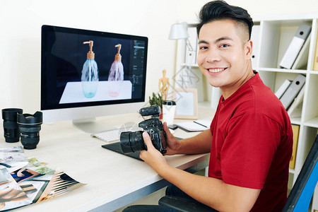 微笑快乐的亚洲年轻摄影师坐在办公桌前图片