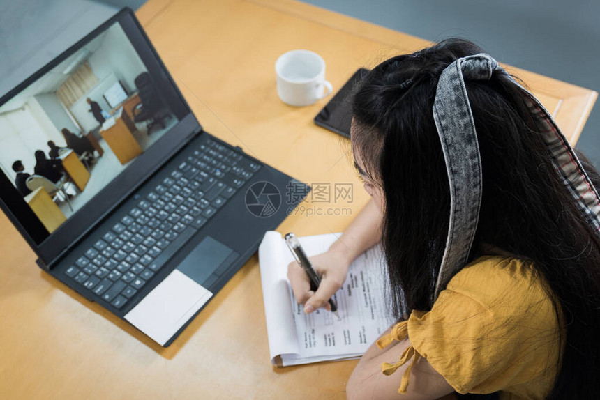 一名青少年学生通过笔记本电脑在线大学生女孩观看在线课程并在笔记本上编写教学大纲远程在线网络研讨会图片