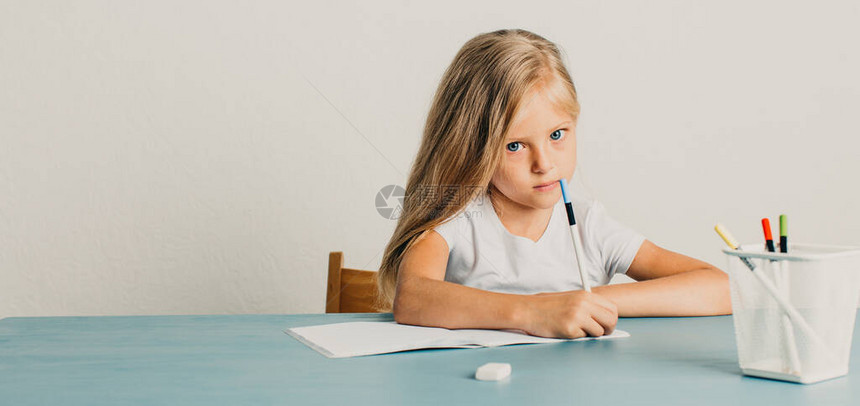 金发女孩坐在桌边在笔记本上写字图片