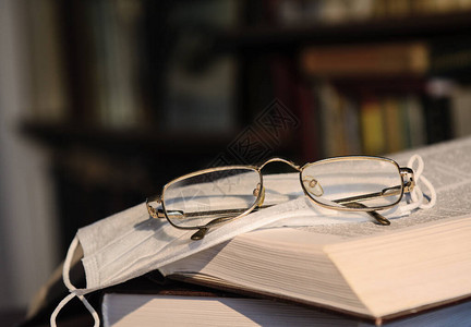 打开的书上有一个金色框架中的医用口罩和眼镜以书架为背景概念培背景图片