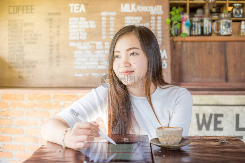 有吸引力的年轻亚洲年轻妇女在咖啡店使用平板电脑图片
