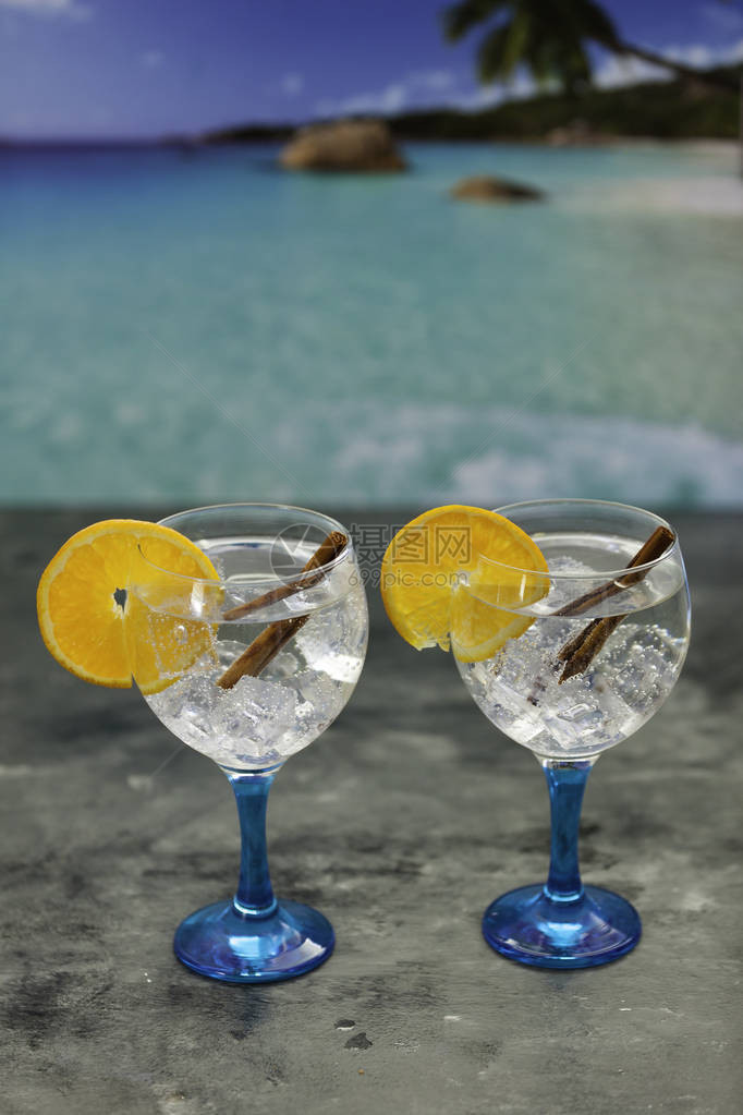 蓝玻璃上两杯加橙片和黑桌肉桂棒的杜松子酒图片