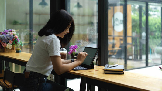 咖啡厅玻璃窗旁坐在桌边的女用数字石板工作的图片