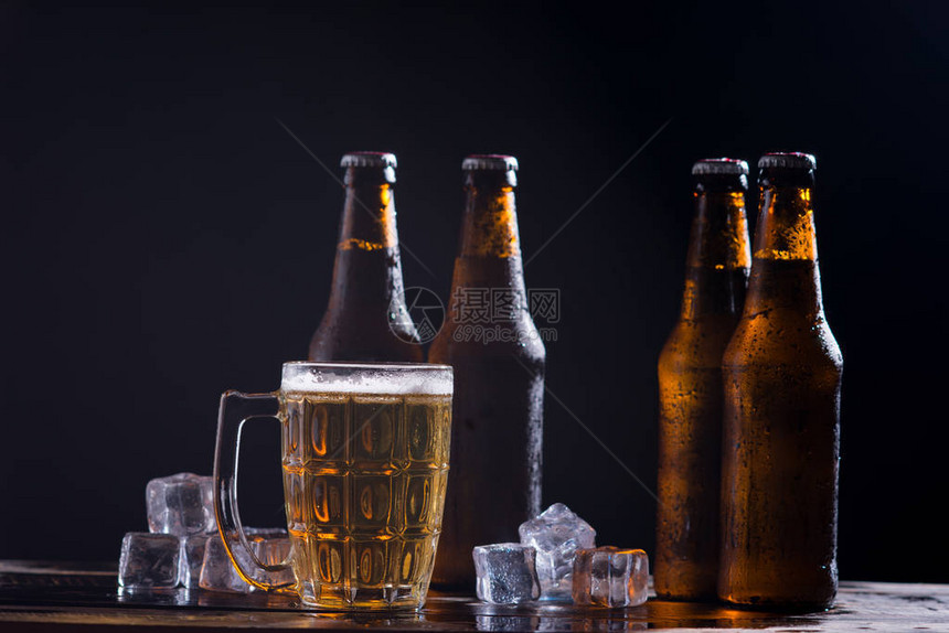 深色背景中带玻璃和冰块的玻璃瓶啤酒图片