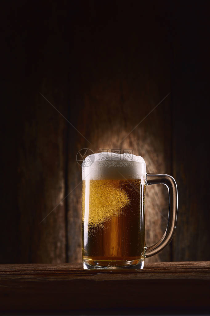 木制背景的木桌上的杯子里的啤酒图片