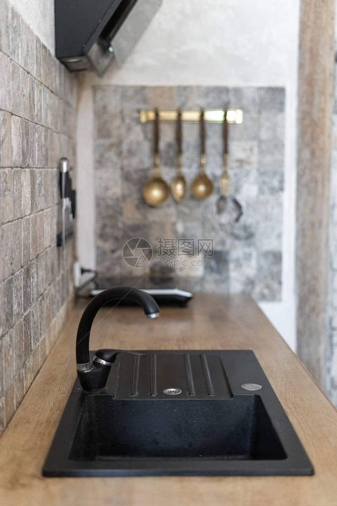 厨房间的垂直照片与舒适的内部木桌上现代水龙头的内置水槽与背景模糊的大理石方砖墙上餐具图片