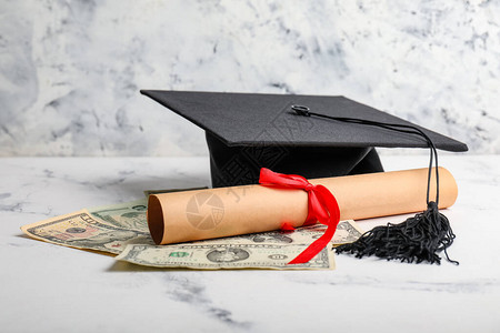 货币文凭和毕业帽子放在桌面图片